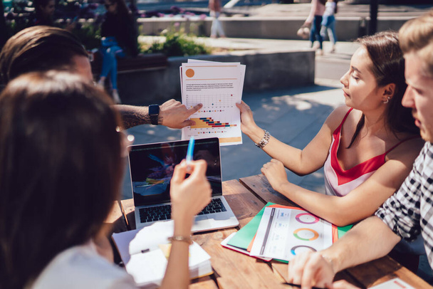 Group of smart freelancers talking and sitting at table with laptop checking documents graphs in outdoor terrace in city in summer - Fotoğraf, Görsel