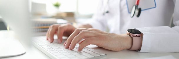 Γιατρός κάθεται στο τραπέζι και πληκτρολογώντας στο πληκτρολόγιο του υπολογιστή closeup - Φωτογραφία, εικόνα