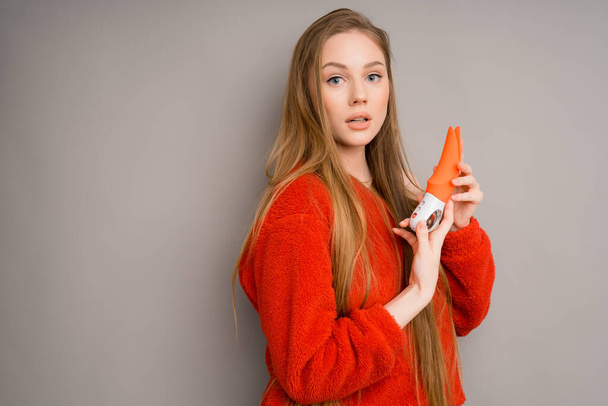 An Italian girl in a red sweater is holding a red vibrator or a dildo for sex.Useful for a sex shop - Фото, изображение