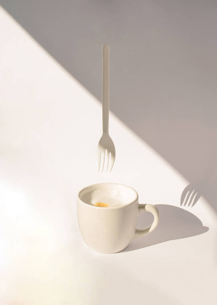 cup of coffee with fork hanging from above.aesthetic abstract idea with shadows - Foto, afbeelding