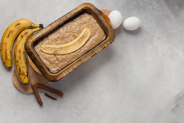 Raw banana bread dough in rectangular shape with ingredients on light background - Zdjęcie, obraz