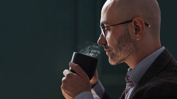 Bald man holding a mug of hot drink and sniffing it - Zdjęcie, obraz