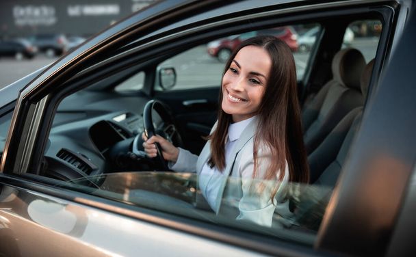 Beautiful happy successful businesswoman is driving a new modern car in good mood. Portrait cute female driver steering car with safety belt - Fotó, kép