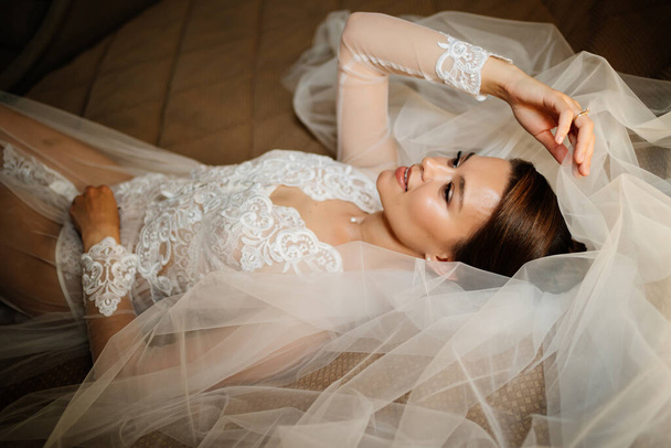 a gentle bride in a lace robe lies in bed on a veil. morning before the wedding. - Foto, Imagem