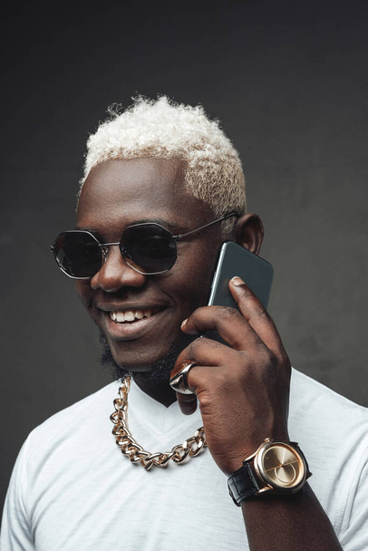 Fröhlicher afrikanischer Mann telefoniert vor grauem Hintergrund - Foto, Bild
