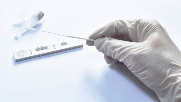  ręka w rękawiczce trzymając pączek bawełny i zestaw do testów antygenowych do sprawdzania COVID-19 lub koronawirusa na białym tle - Zdjęcie, obraz