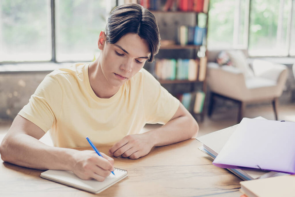 Portrait of attractive focused guy writing list essay doing homework preparing academic test exam indoors - Фото, зображення