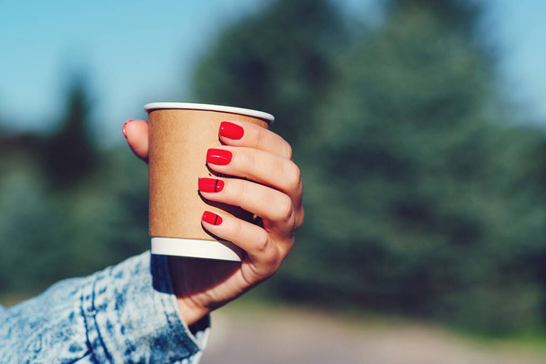 Papieren koffiebeker in vrouwenhanden met perfecte manicure. Vrouwelijke hand met koffie afhalen. Een vrouw met een beker in haar handen. Afhaalkoffie drinken. - Foto, afbeelding