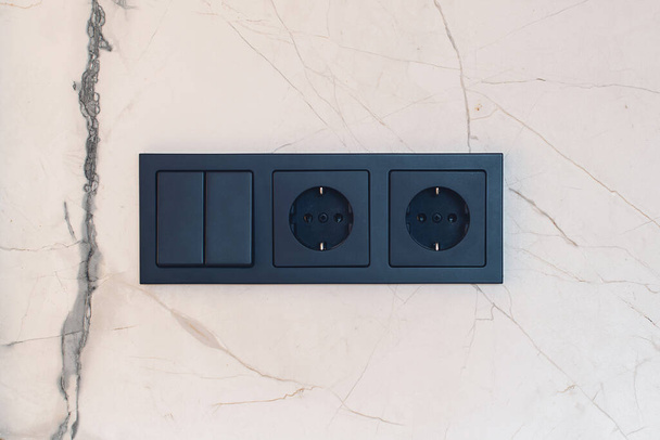 New black switch and socket on the marble wall. Kitchen background. Electric light switch and socket on the empty wall. Electrical power socket and plug switched. - Foto, Bild