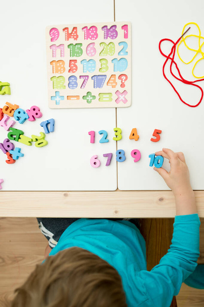 kid learning numbers through game. Sensory activity with wooden numbers and shoe laces. Educations at home, pre-school education, Montessori methodology. sequence of numbers, arithmetic problems. - Photo, image