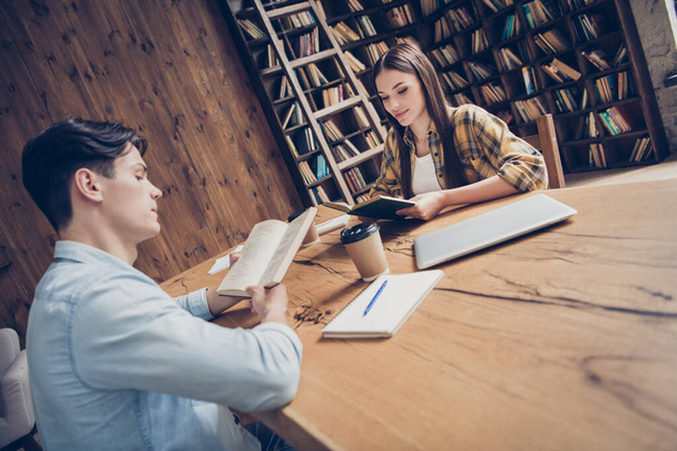 Portrait of two attractive focused people learners reading paper book dictionary at loft industrial interior indoors - Фото, зображення