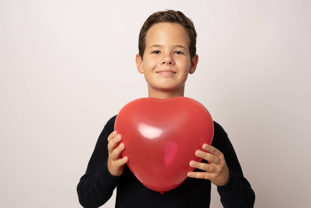 Fiatal szép fiú gazdaság szív alakú párna felett fehér háttér - Fotó, kép