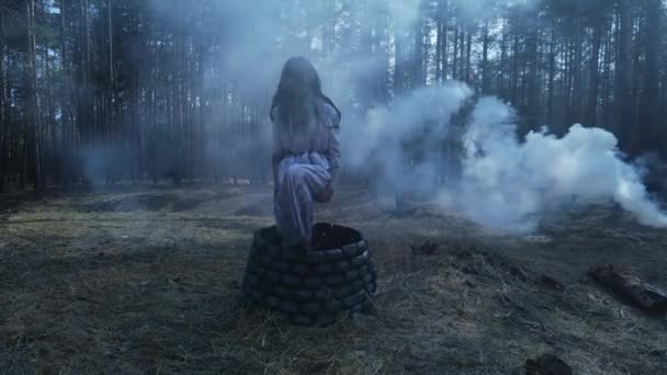 Dívka s dlouhými černými vlasy v obrazu strašidelného ducha zombie vylézá z kamenné studny a kráčí lesem proti kouři pozadí. Halloween koncept. - Záběry, video