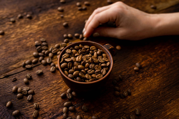 Coffee beans full cup and female hands on brown old wooden background. - Foto, immagini