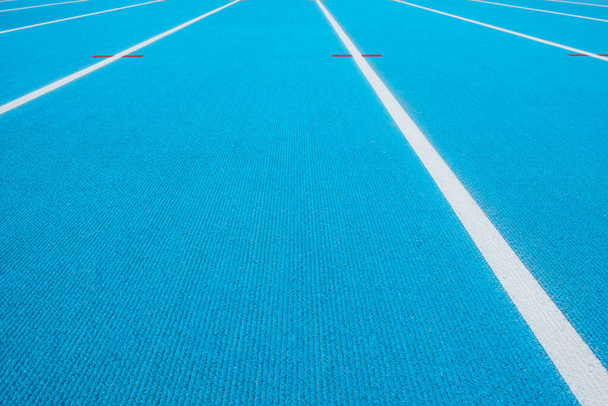 Sportowa przeszłość. Niebieski tor biegowy z białymi liniami i czerwonym znakiem na stadionie sportowym. Widok z góry - Zdjęcie, obraz