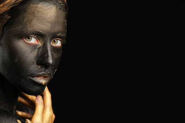 Όμορφη νεαρή γυναίκα με μαύρη και χρυσή μπογιά στο σώμα της σε σκούρο φόντο - Φωτογραφία, εικόνα