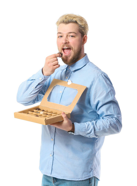 Handsome young man with box of chocolate candies on white background - Photo, Image