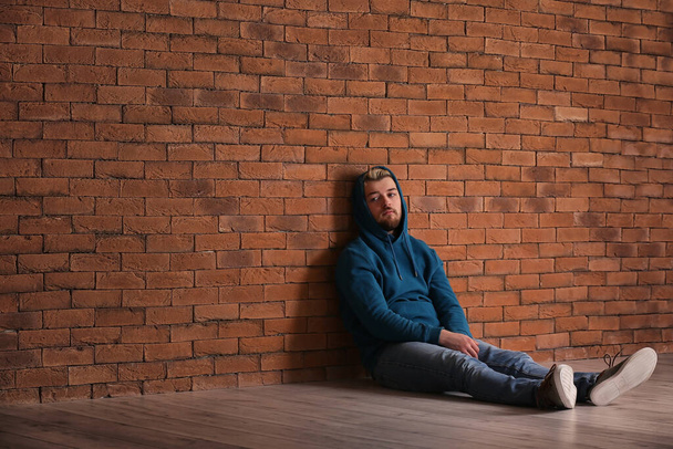 Депрессивный молодой человек сидит у кирпичной стены
 - Фото, изображение