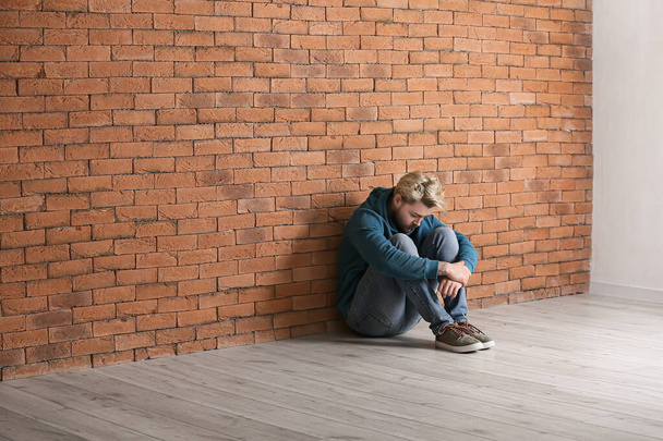 Depressed young man sitting near brick wall - Fotoğraf, Görsel