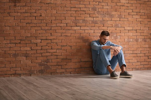 Μελαγχολικός νεαρός άνδρας που κάθονται κοντά σε τοίχο από τούβλα - Φωτογραφία, εικόνα