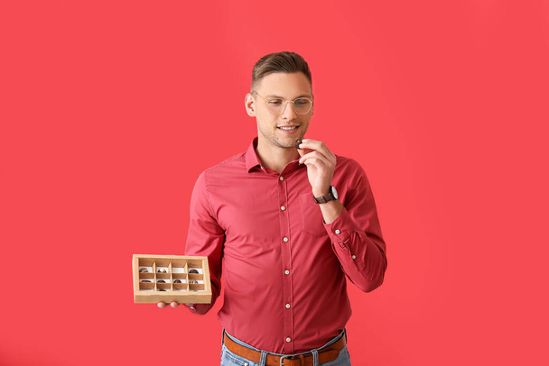 Bonito jovem com caixa de doces de chocolate no fundo de cor - Foto, Imagem