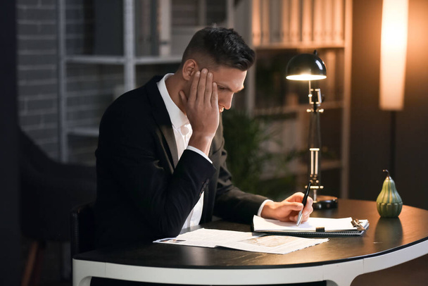 Depressed young businessman in office late in evening - Foto, afbeelding