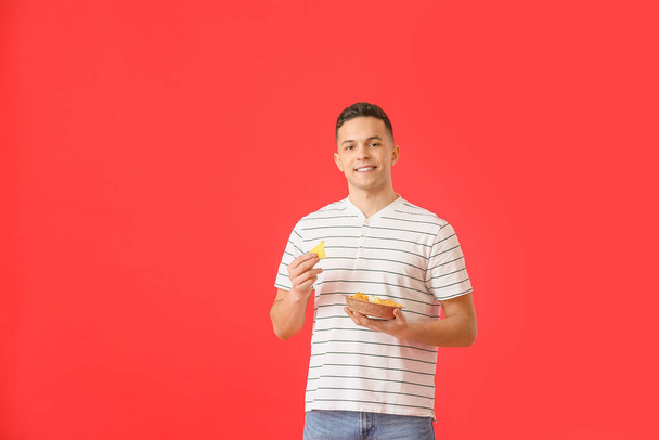 Jóképű fiatalember ízletes nachos színes háttér - Fotó, kép