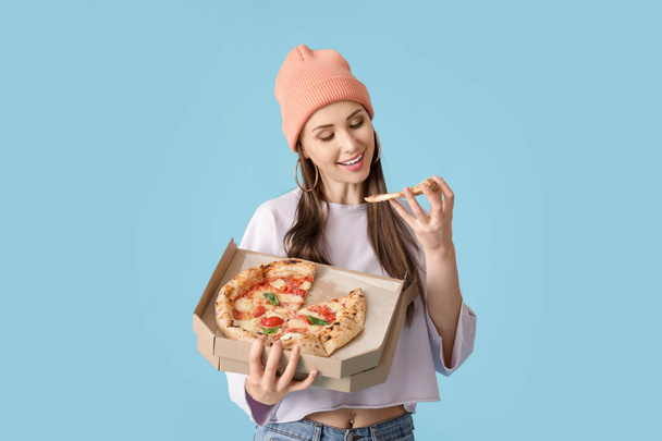 美しい若い女性食べるおいしいピザ上の色の背景 - 写真・画像