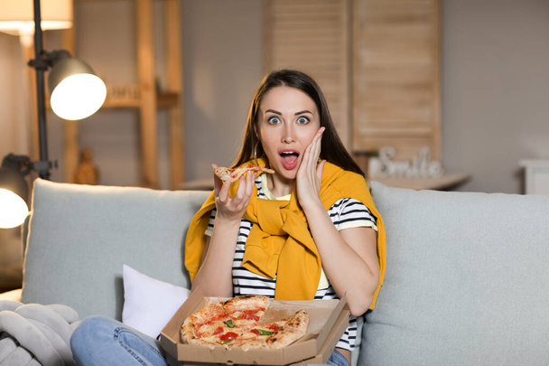 Hermosa mujer joven comiendo sabrosa pizza mientras ve la televisión en casa por la noche - Foto, Imagen