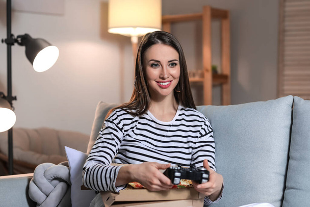 Hermosa mujer joven comiendo sabrosa pizza mientras juega videojuego en casa por la noche - Foto, imagen
