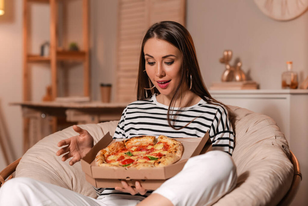 Beautiful young woman eating tasty pizza at home in evening - Photo, Image