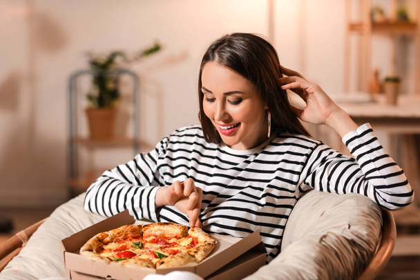 Beautiful young woman eating tasty pizza at home - Valokuva, kuva