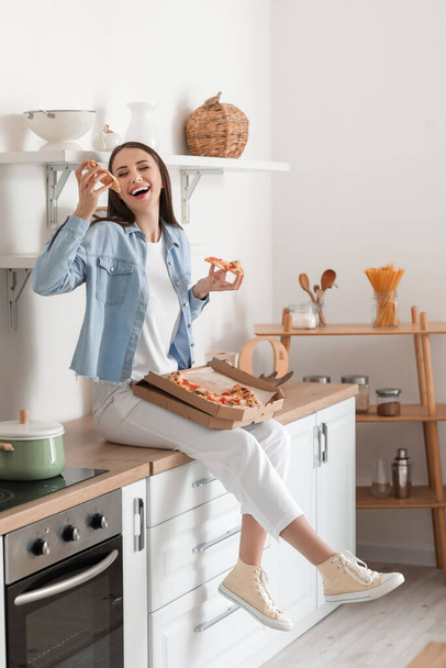 Beautiful young woman eating tasty pizza in kitchen - Фото, зображення
