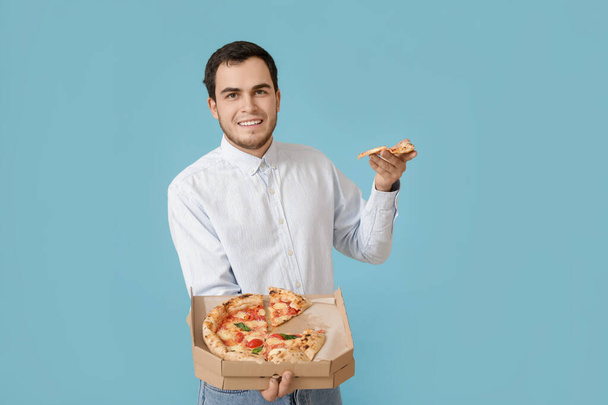 Красивий молодий чоловік їсть смачну піцу на кольоровому фоні
 - Фото, зображення