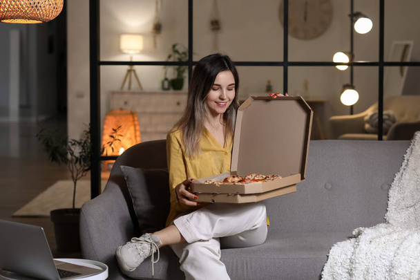 Beautiful young woman eating tasty pizza at home in evening - Foto, afbeelding