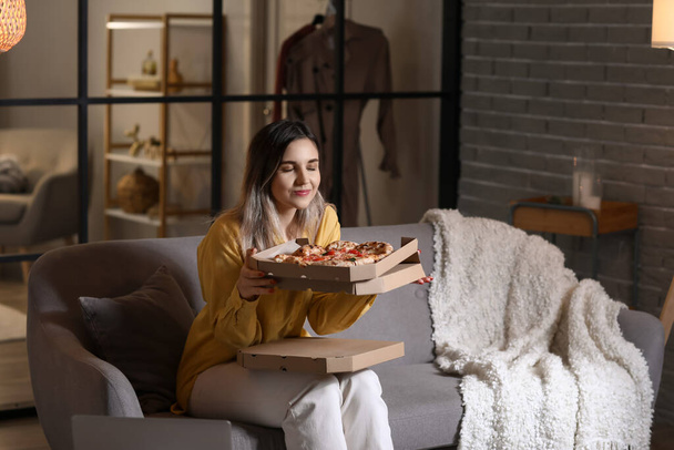 Beautiful young woman eating tasty pizza at home in evening - Foto, Bild