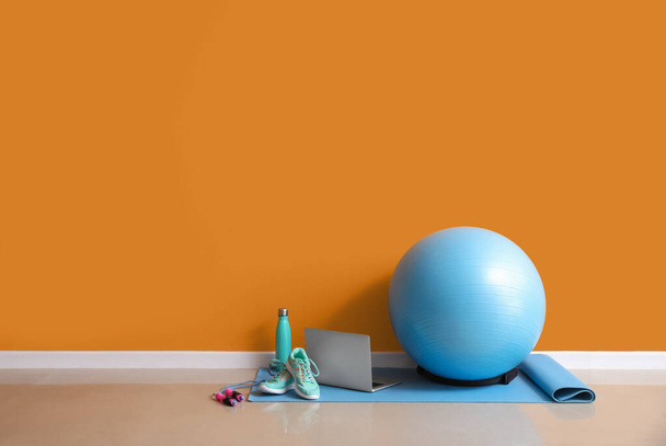 Set of sports equipment and laptop on floor near color wall - Фото, зображення