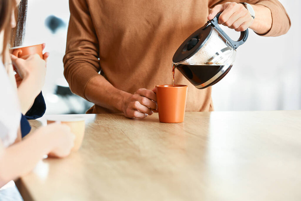 Young man pouring coffee into cup in office - Photo, image