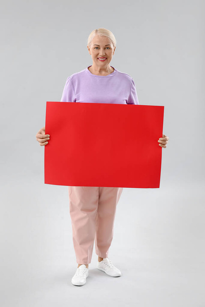 Mature woman with blank poster on light background - Фото, изображение