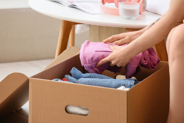 Молодая женщина упаковывает одежду в коробку дома, крупным планом - Фото, изображение