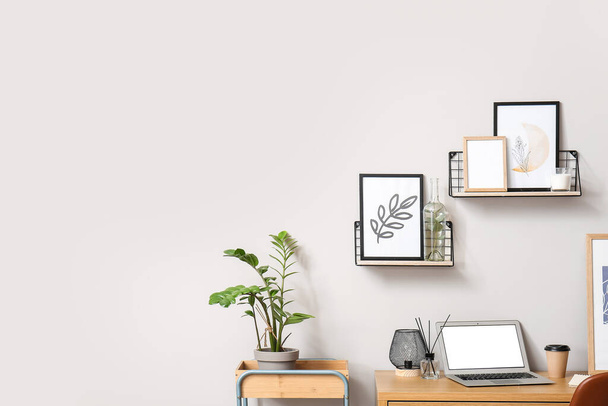Modern workplace with laptop and frames near light wall - Fotografie, Obrázek