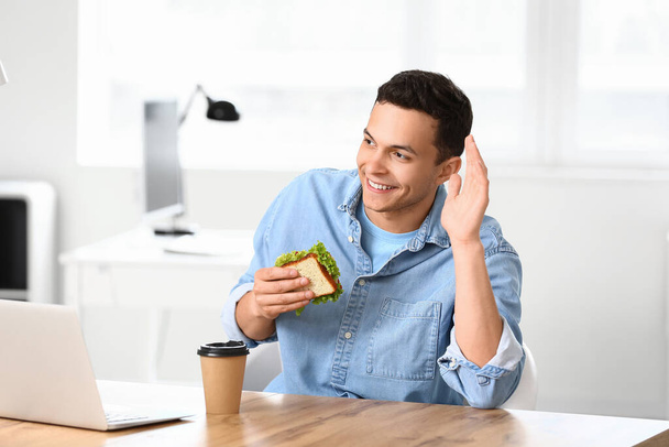 Young man with tasty sandwich in office - Photo, Image