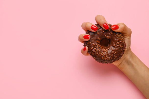 Женская рука с красивым маникюром держа вкусный пончик на цветном фоне - Фото, изображение