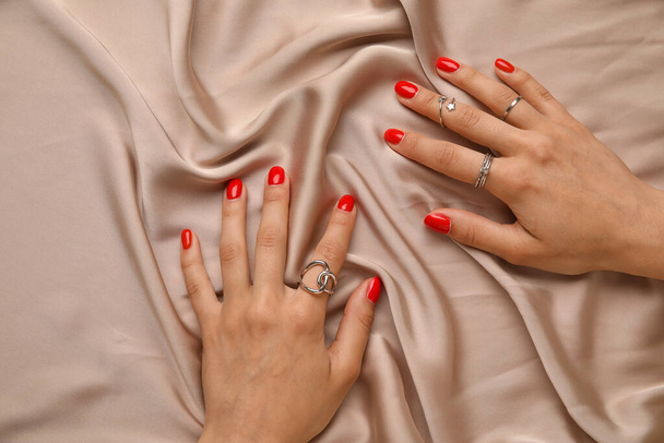 Женские руки с красивым маникюром и ювелирными украшениями на фоне цветной ткани - Фото, изображение