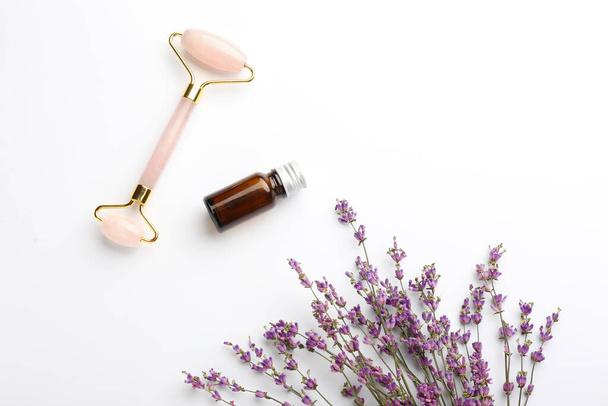 Herramienta de masaje facial, botella de aceite esencial y flores de lavanda sobre fondo blanco - Foto, Imagen