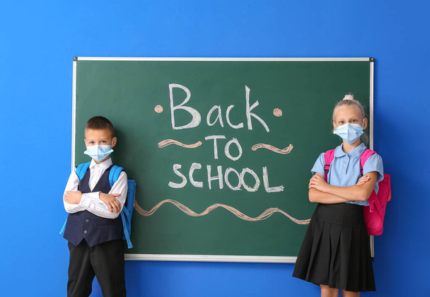 Žáci v lékařských maskách v blízkosti tabule na barevném pozadí - Fotografie, Obrázek