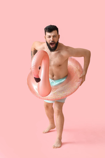 Funny young man with inflatable ring on color background - Foto, Bild