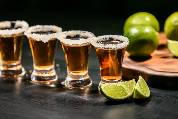 Tomas de tequila sabroso con lima sobre fondo oscuro - Foto, Imagen