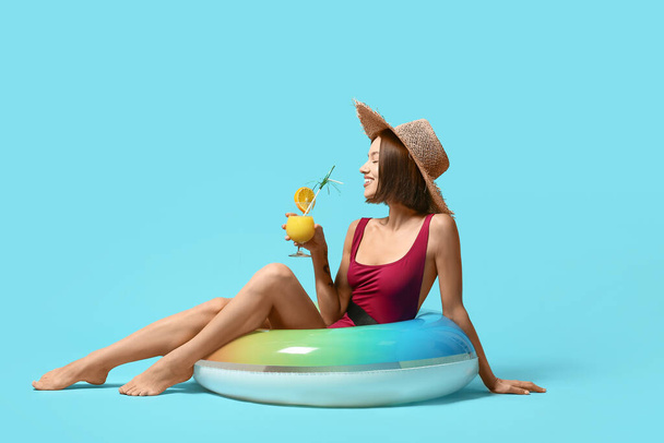 Young woman with cocktail and inflatable ring on color background - Photo, Image