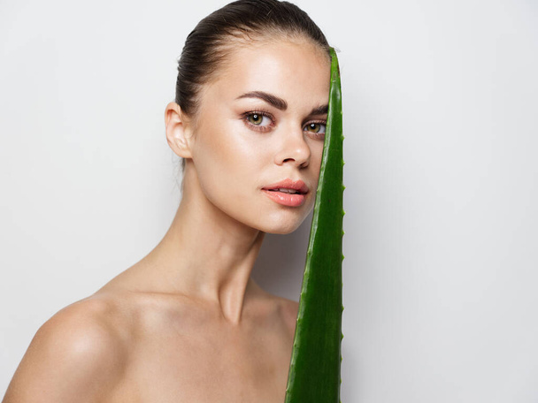 young woman with clean skin and bare shoulders holding an aloe leaf in her hand - Foto, Imagem